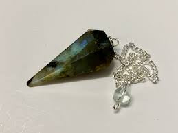 A stunning labradorite pendulum, with its teardrop-shaped stone exhibiting a captivating play of blue, green, and gold iridescence. The stone is attached to a delicate silver chain, making it perfect for pendulum dowsing or as a beautiful piece of crystal jewelry.